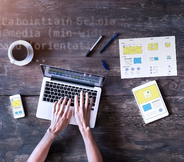 A woman working on her laptop and tablet at a wooden table, representing a web design agency in Dubai